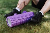 pexels-photo-4378850-4378850 Black sneakers and purple foam roller on grass, outdoor fitness scene.